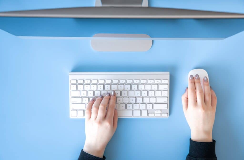 Top view, female hands work at the computer, blue background.
