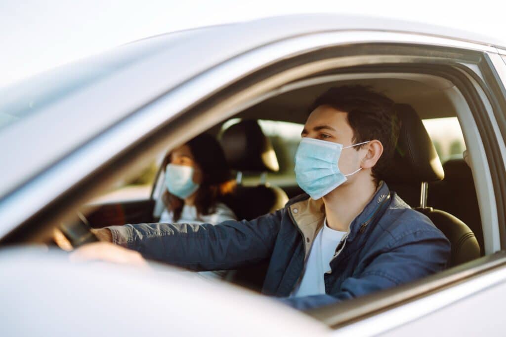 Woman wearing a medical sterile mask in a taxi car on a backseat looking sideway out of open window.