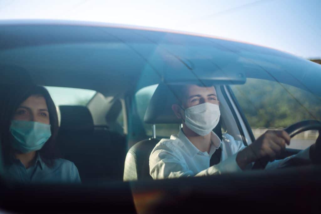 Young man and woman driving in a car during coronavirus quarantine in medical masks. Safe taxi