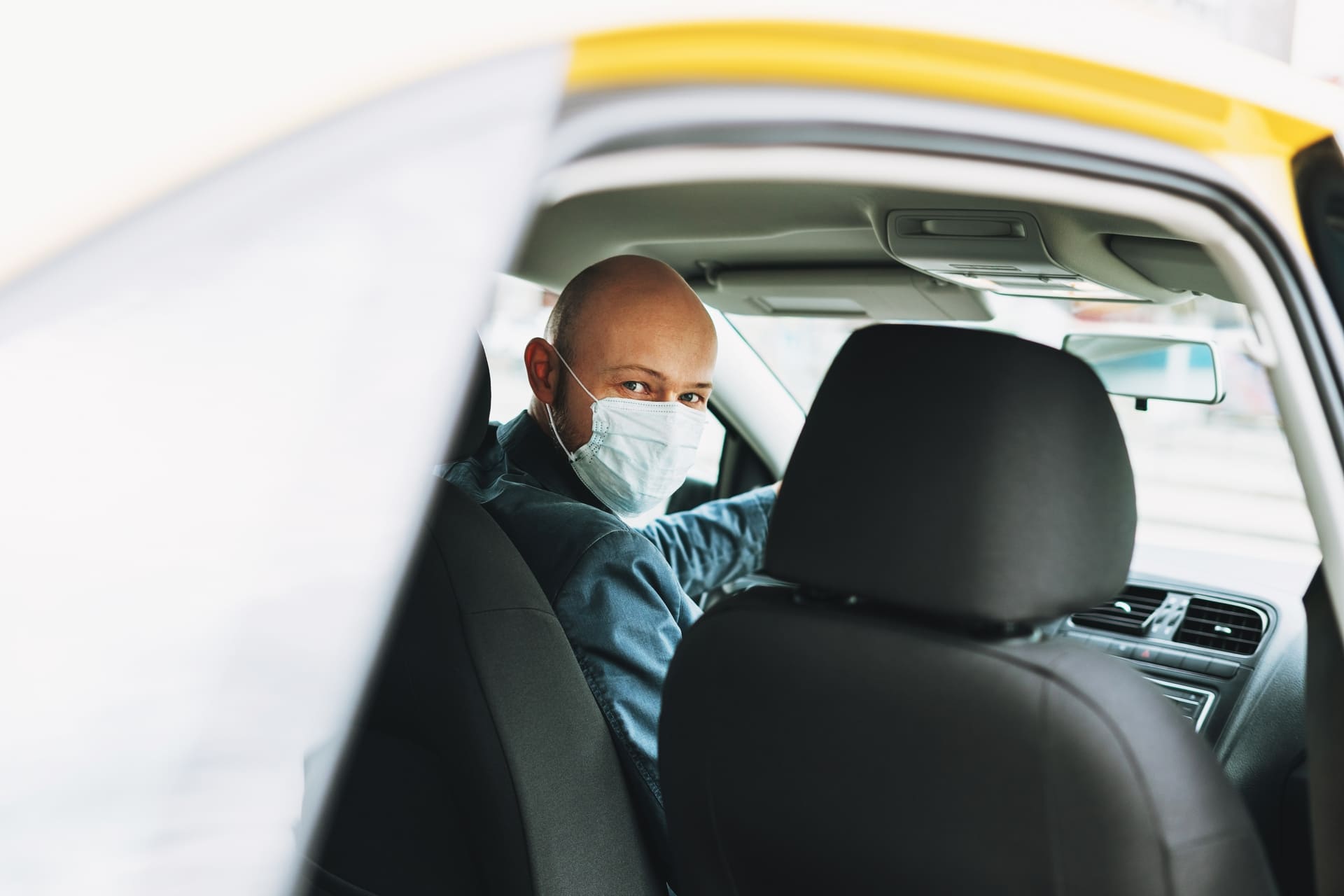 bald man taxi driver in medical face mask inside